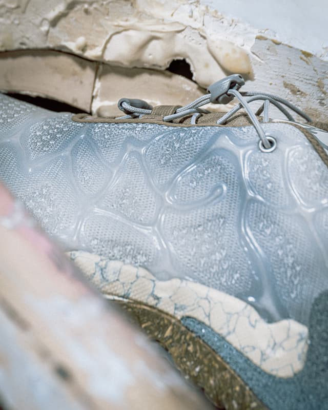 Close-up of a sneaker with a translucent wavy upper, grey toggle laces, and a sole featuring cracked cream and dark textures.