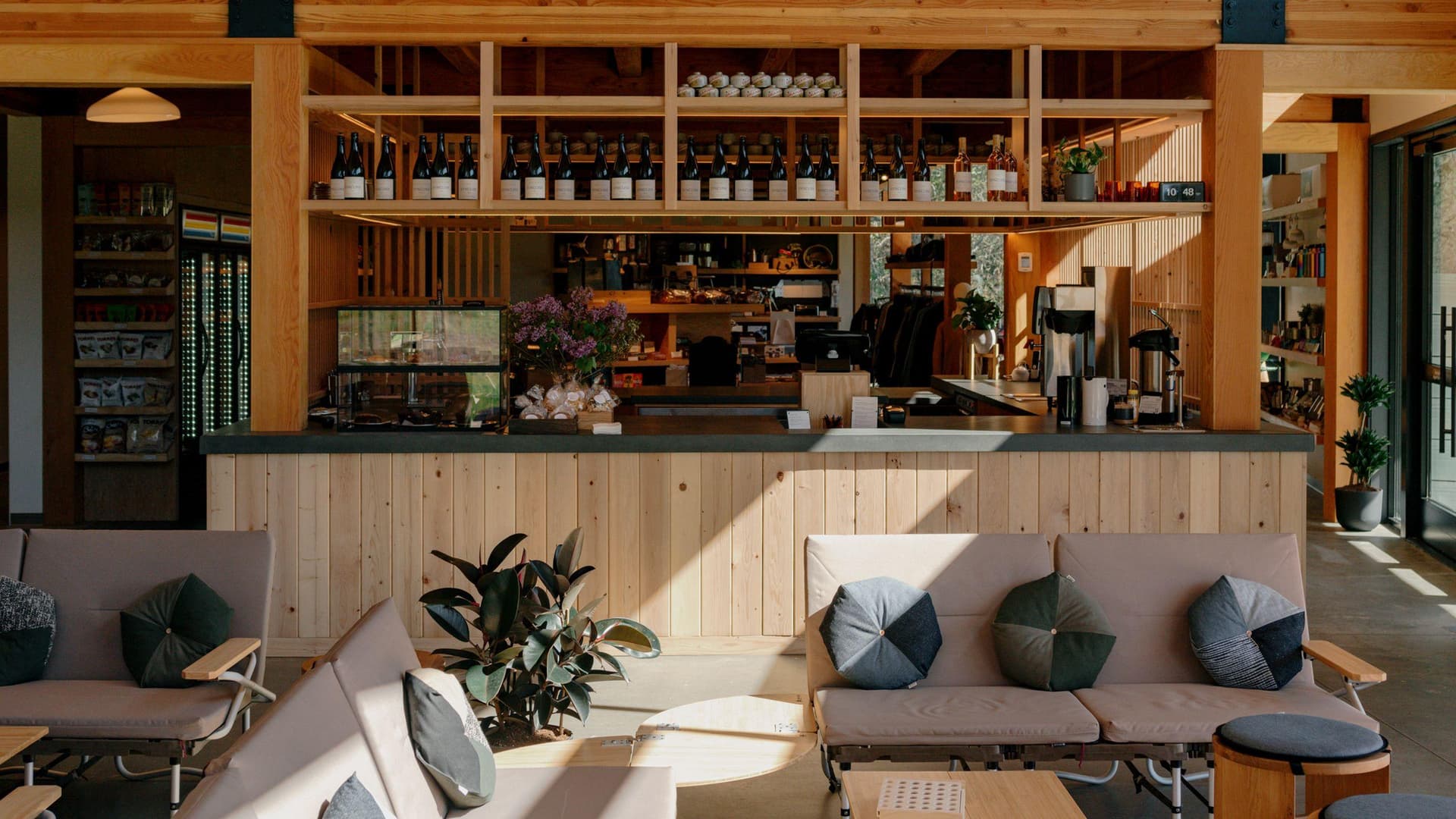 A sunlit cafe interior with a wooden bar, shelves of bottles, and comfortable seating.