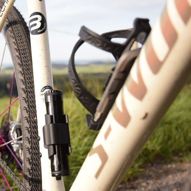 A black bicycle pump and water bottle cage on a cream bicycle frame outdoors.