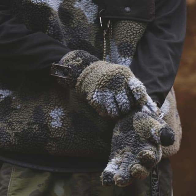 A person in a fuzzy green, black, and light grey patterned sherpa jacket and mittens.