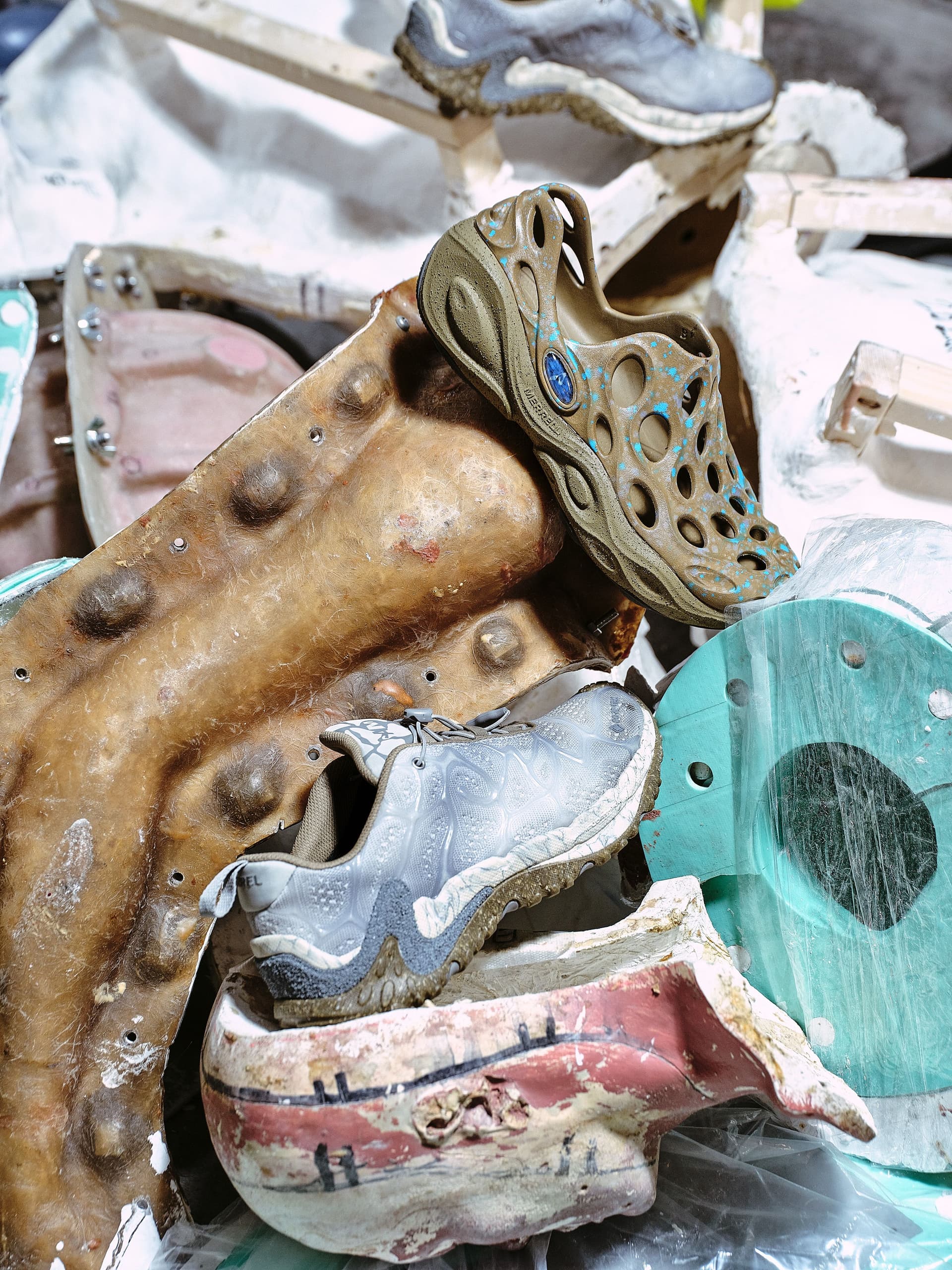 Two worn shoes, a tan perforated sandal and a gray sneaker, rest on a pile of textured plaster casts and sculptural fragments.