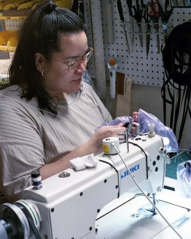 A person wearing glasses sews fabric on an industrial sewing machine.