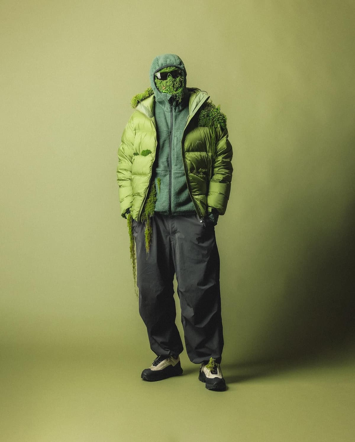 A person in green outdoor gear with head and shoulders covered in moss and sunglasses.