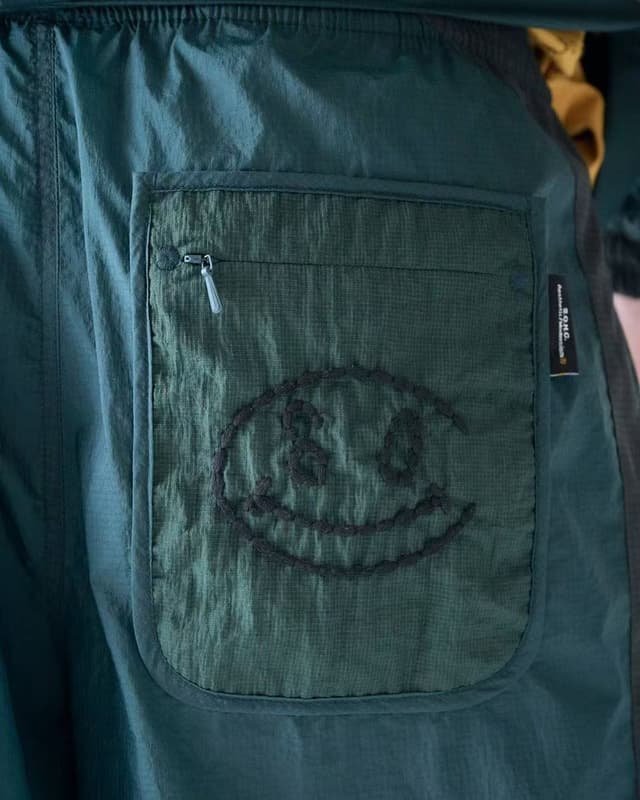 Dark green clothing pocket with a zipper, an embroidered abstract smiley face, and a "B.O.N.G." tag.