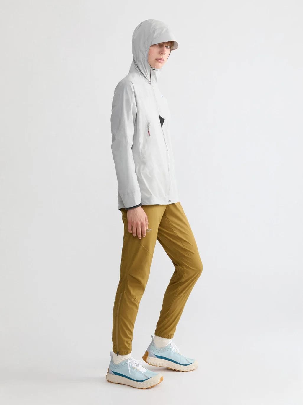 Person wearing a light grey hooded jacket, brown pants, and light blue sneakers.