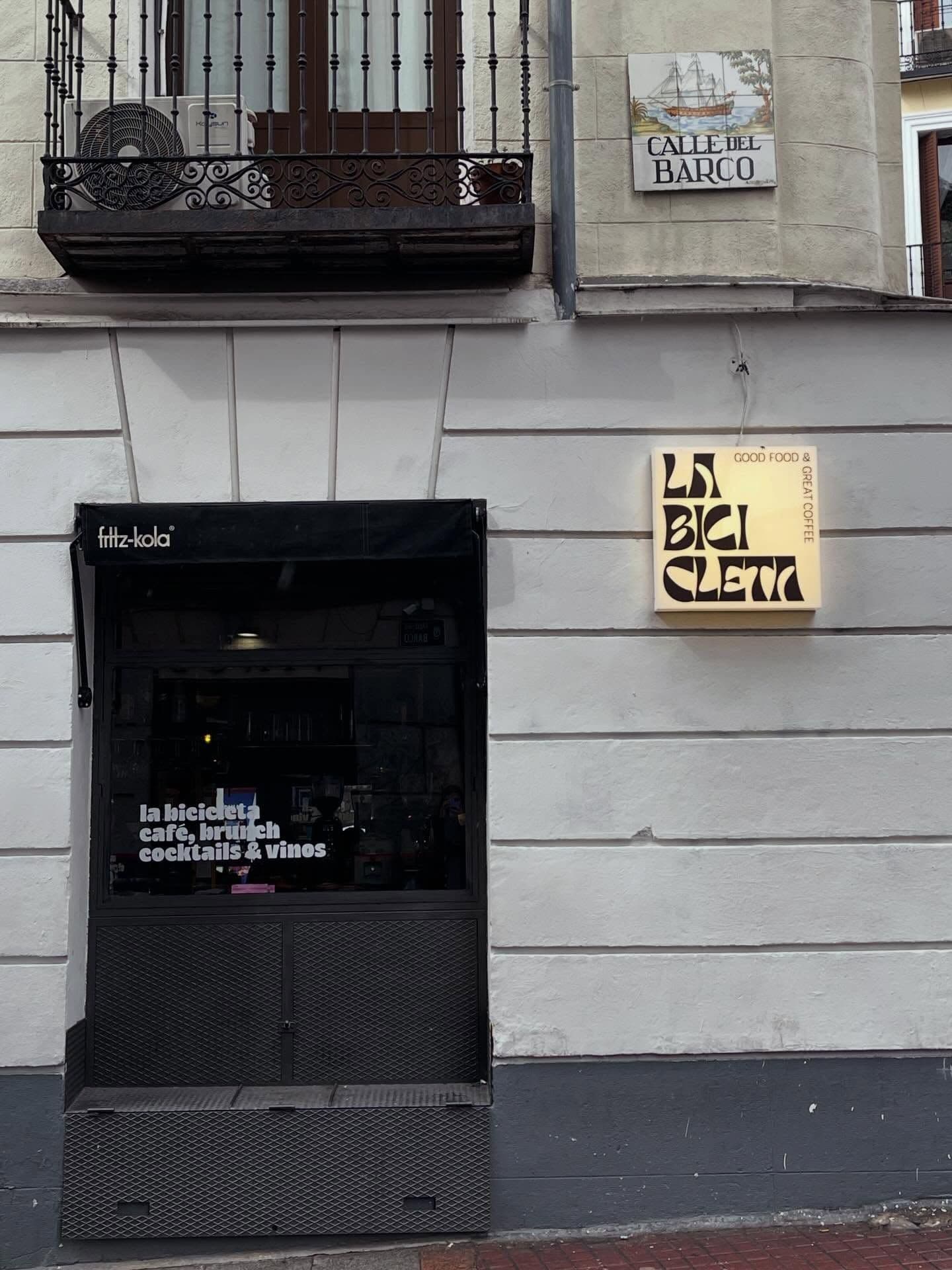 Facade of a building with "La Bicicleta" cafe entrance, an illuminated sign, and a "Calle del Barco" street tile above. An ornate balcony is visible on the upper left.