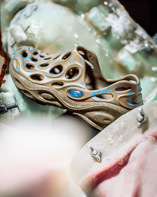 A tan Merrell Hydro Moc shoe with blue splatters, resting on a textured surface.