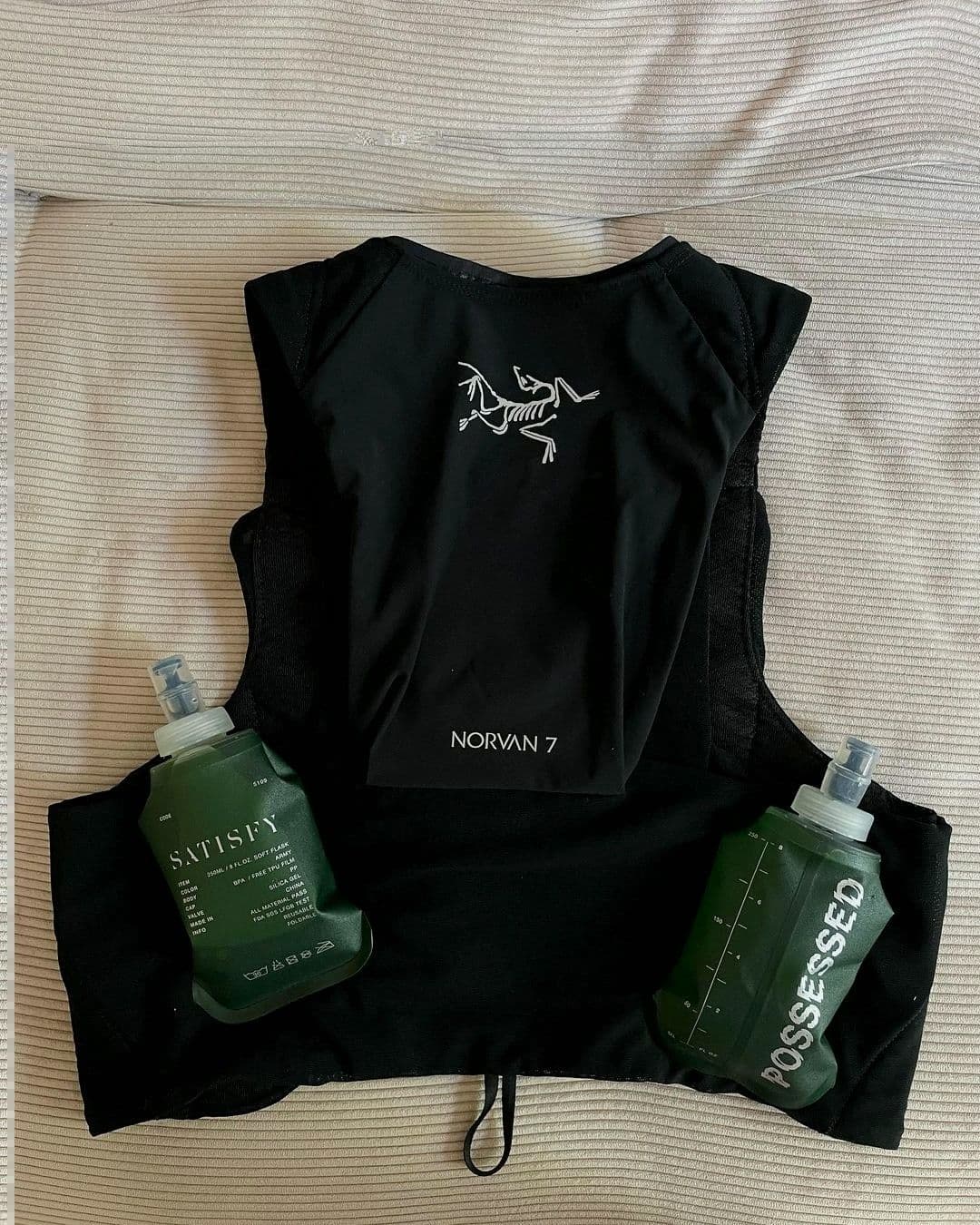 A black Arc'teryx Norvan 7 running vest with two green soft flasks labeled "Satisfy" and "Possessed".
