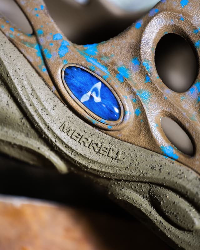 Close-up of a brown Merrell shoe with blue splatter design and logo.