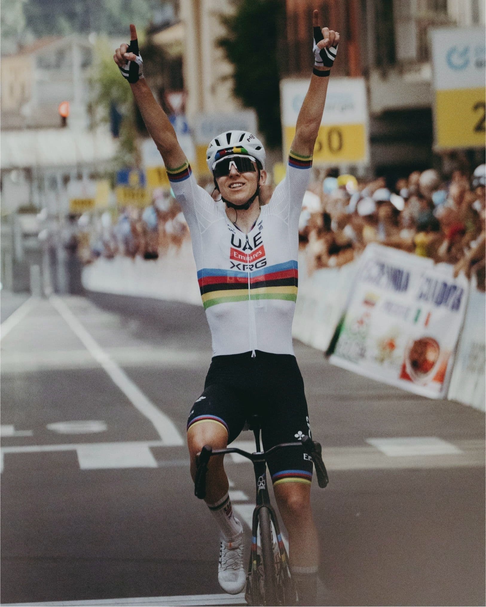 Male cyclist in a world champion's jersey raising his arms in victory on a road.