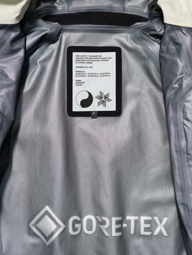 Inside of a gray jacket showing a white product label from Our Legacy / Goldwin and a large Gore-Tex logo.