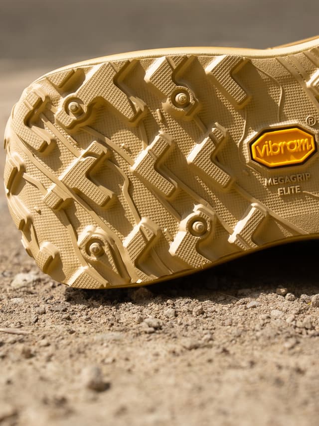 Tan shoe sole with rugged tread and Vibram Megagrip Elite branding, on dirt.