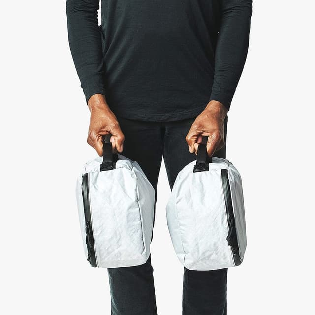 A person in dark clothing holds two white, crinkled bags with black handles.
