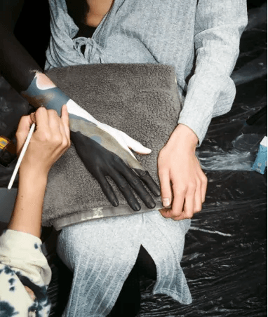 An artist applies black, white, and muted gold body paint to a person's arm and hand.