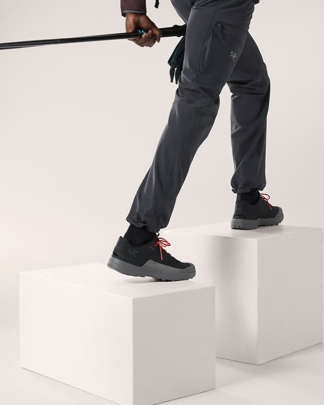A person in gray hiking pants and black shoes steps onto white blocks while holding a trekking pole.