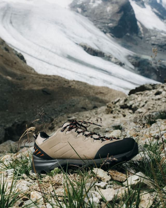 A tan hiking shoe rests on rocky ground with a large glacier in the background.