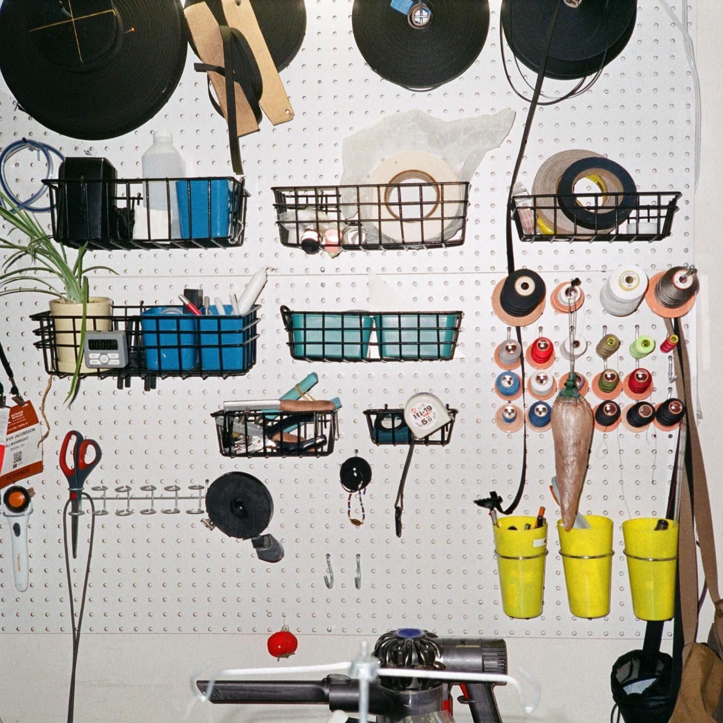A white pegboard wall displaying neatly organized craft and sewing supplies, including spools of thread and ribbon, tools, and baskets.