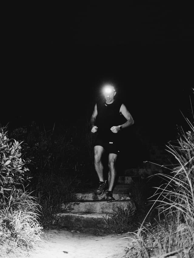 A person wearing a headlamp runs down dark outdoor stairs at night.
