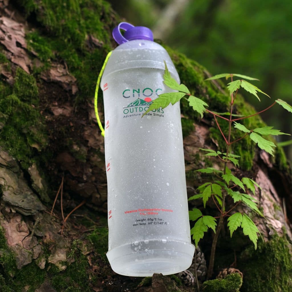 A semi-transparent CNOC OUTDOORS water bottle with a purple cap hangs against a mossy tree trunk.