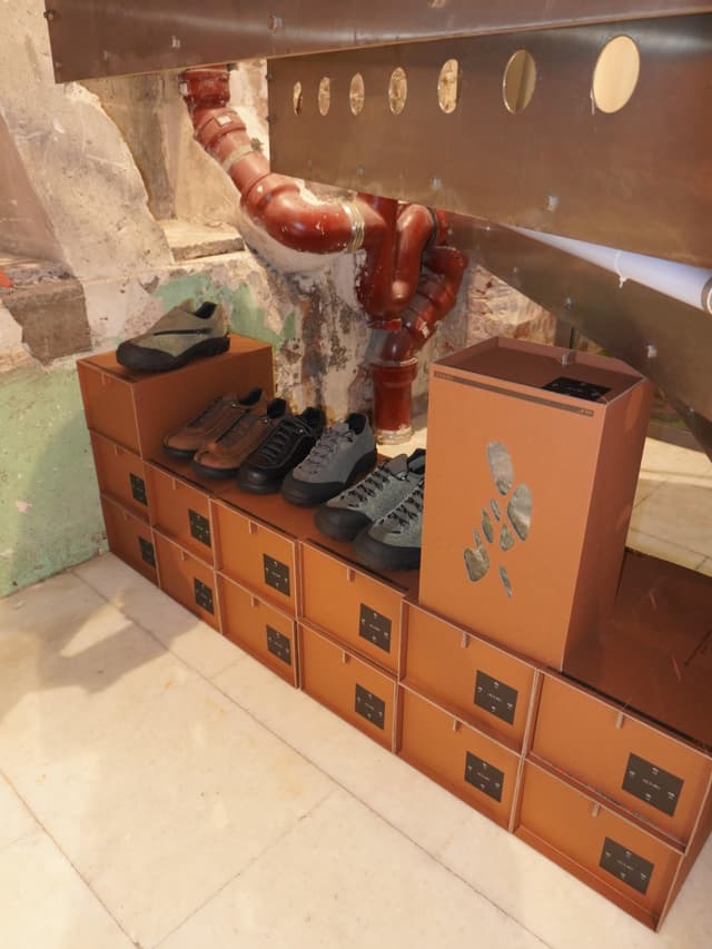 Shoes displayed on stacked cardboard boxes in a raw, industrial space with exposed pipes.
