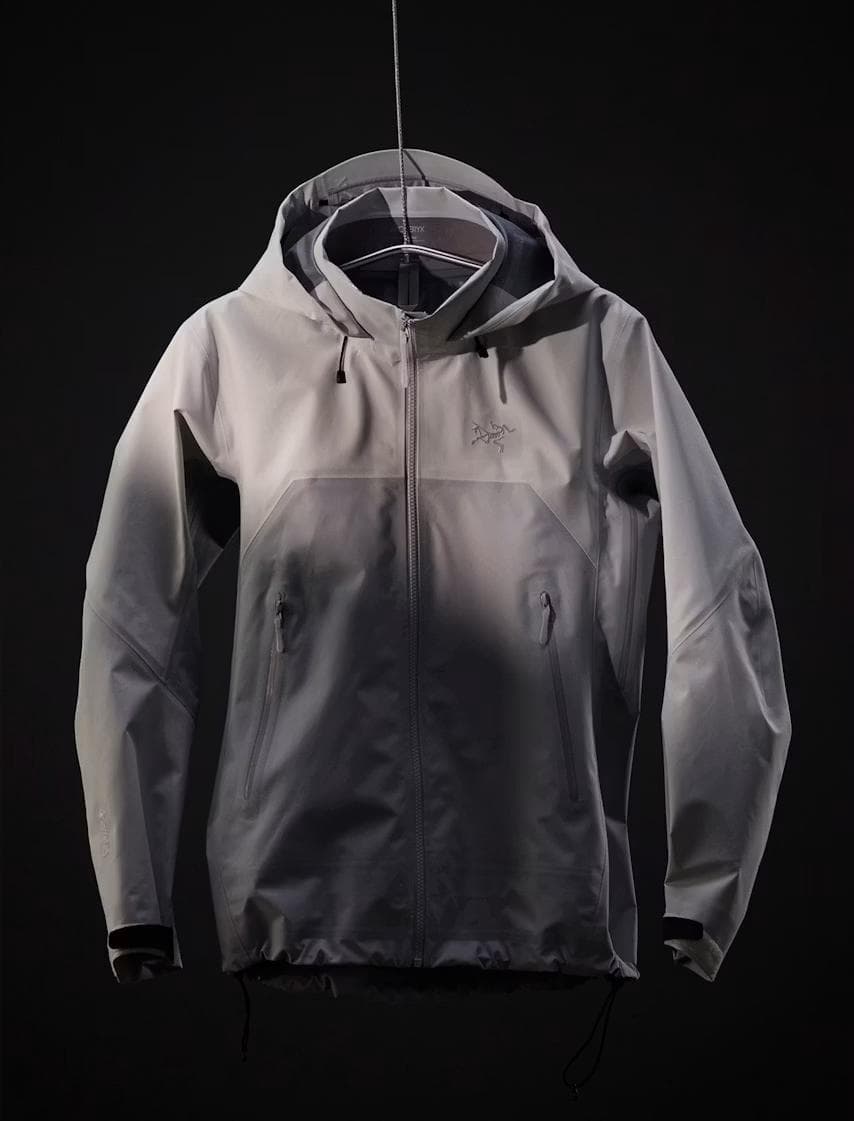 A light gray Arc'teryx hooded jacket hangs against a dark background.