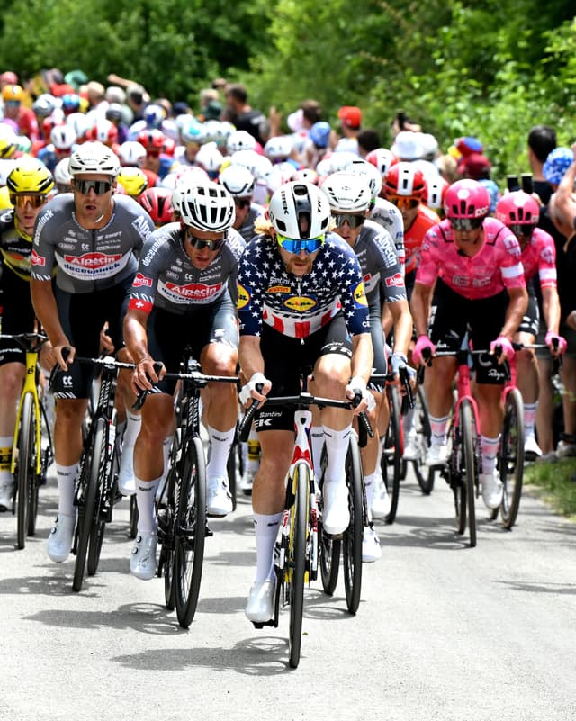 A group of road cyclists race, with one rider in an American flag jersey at the front.