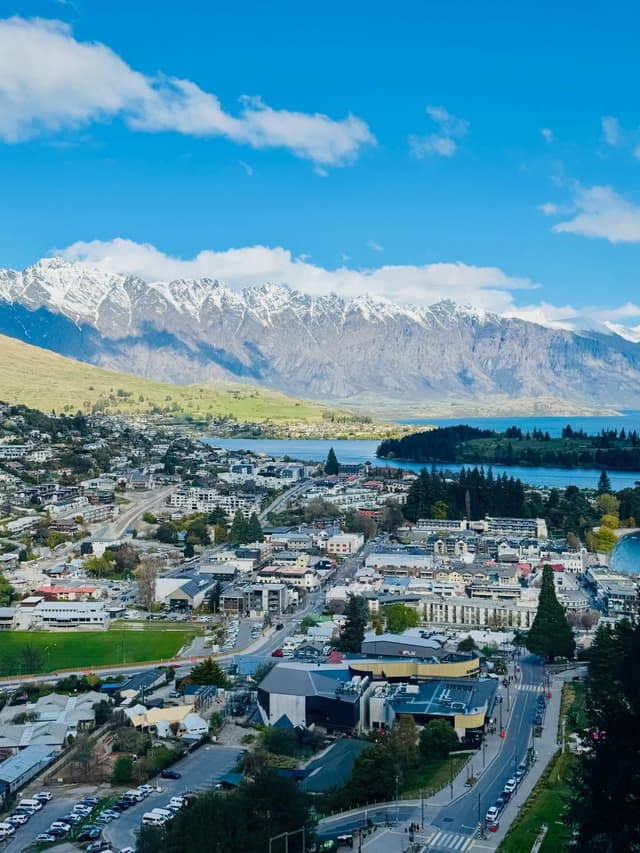 Aerial view of Queenstown, New Zealand, with a town, lake, and snow-capped mountains.