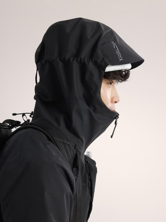 A person in profile wearing a black Arc'teryx hooded jacket with the hood up, and a backpack.