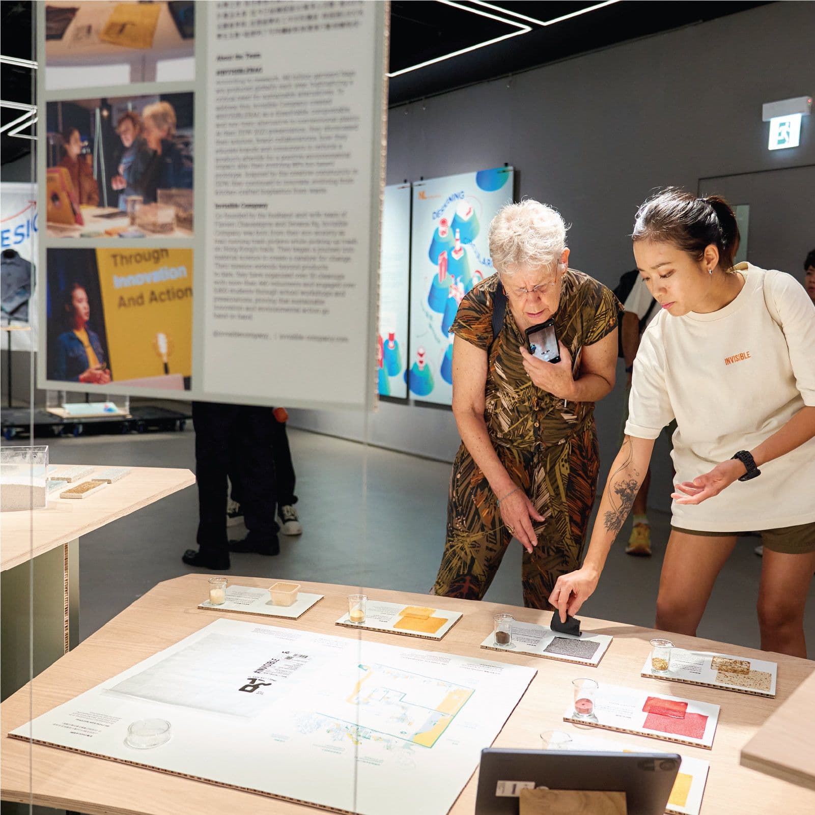 Two women examining an interactive exhibit on a table in a bright modern gallery.