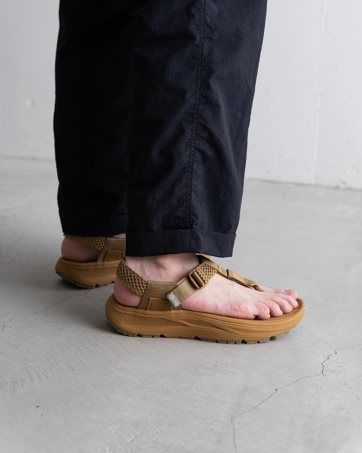 A person's legs wearing black pants and tan sandals with thick soles.