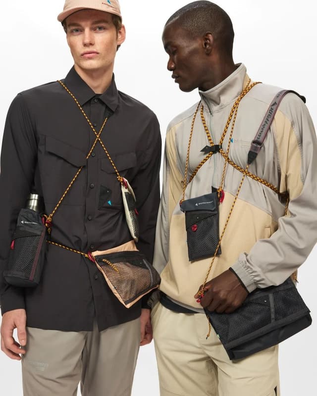 Two men in outdoor-style clothing showcasing modular utility bags and a bottle holder attached with bright orange cords.