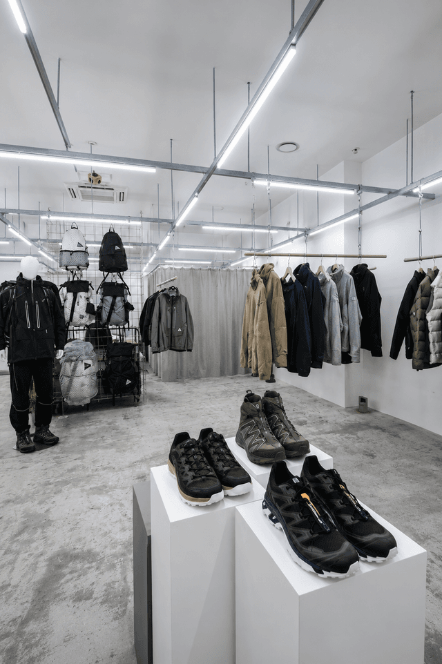 Modern retail store interior displaying outdoor apparel, backpacks, and footwear on mannequins, racks, and pedestals.