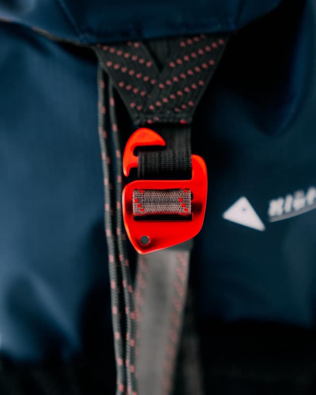 A bright orange plastic buckle secures a black strap with red flecks against a dark blue fabric background.