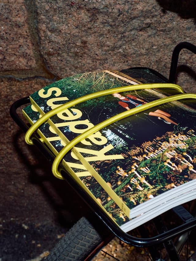Magazines titled "Superficial" with a forest scene cover, secured by a yellow bungee cord on a bike rack.