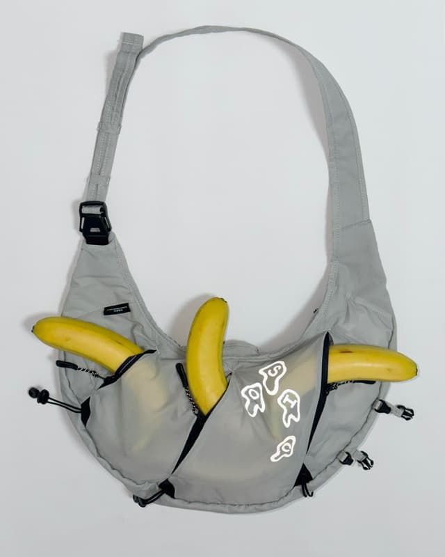A light gray sling bag with three yellow bananas stored in its pockets.
