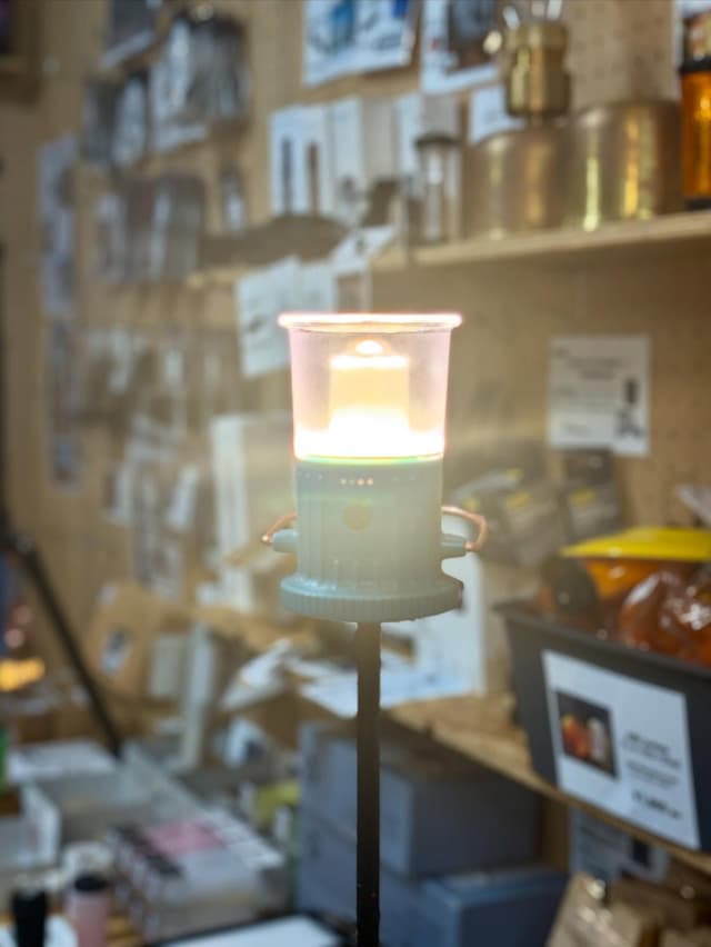 A glowing portable lantern on a stand in a blurry room.