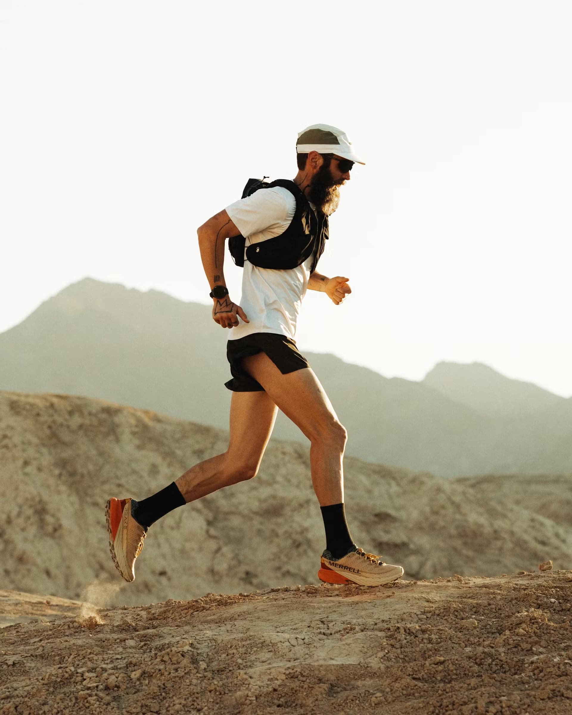 A bearded man in running gear trail running on a dusty desert path.