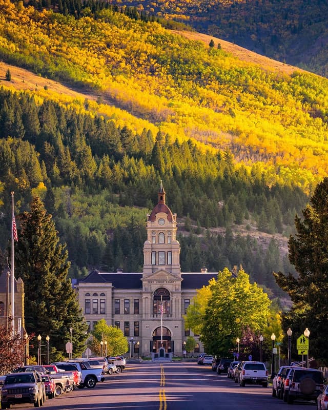 Deer Lodge County Courthouse at the end of a street, backed by a mountain covered in brilliant yellow autumn foliage.