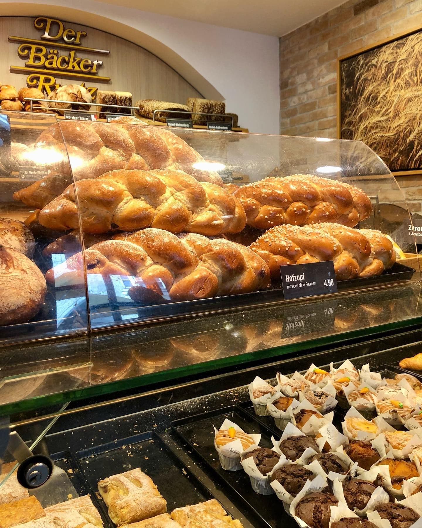 A bakery display case features golden-brown braided Hefezopf breads, muffins, and pastries.