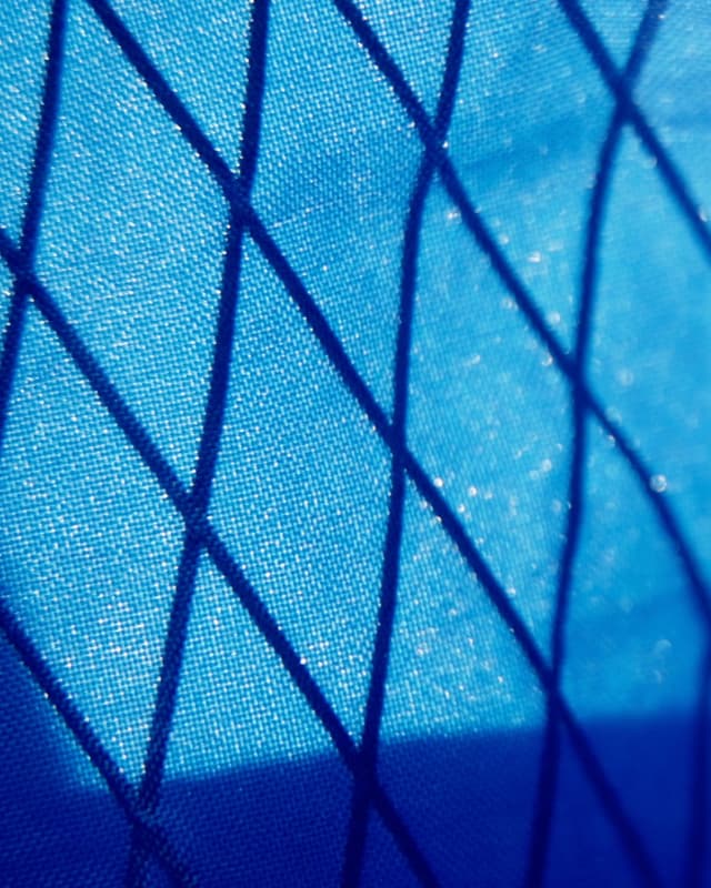 Close-up of blue fabric with a dark diamond grid pattern.