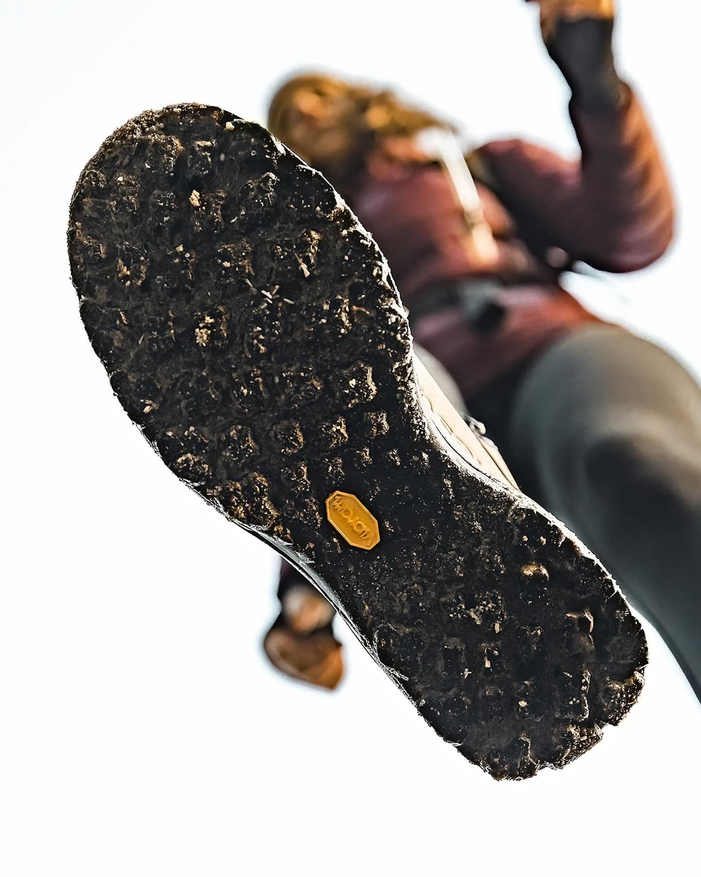 Underside of a dirty shoe sole with a Vibram logo, viewed from a low angle as a person steps.