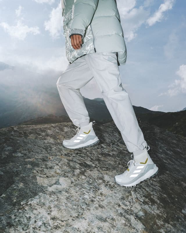 A person in light grey outdoor gear and trail shoes walks up a rocky mountain.