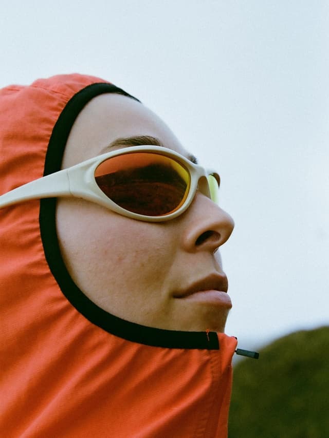 A person in a red hood and white-framed orange-lens sunglasses looks up.