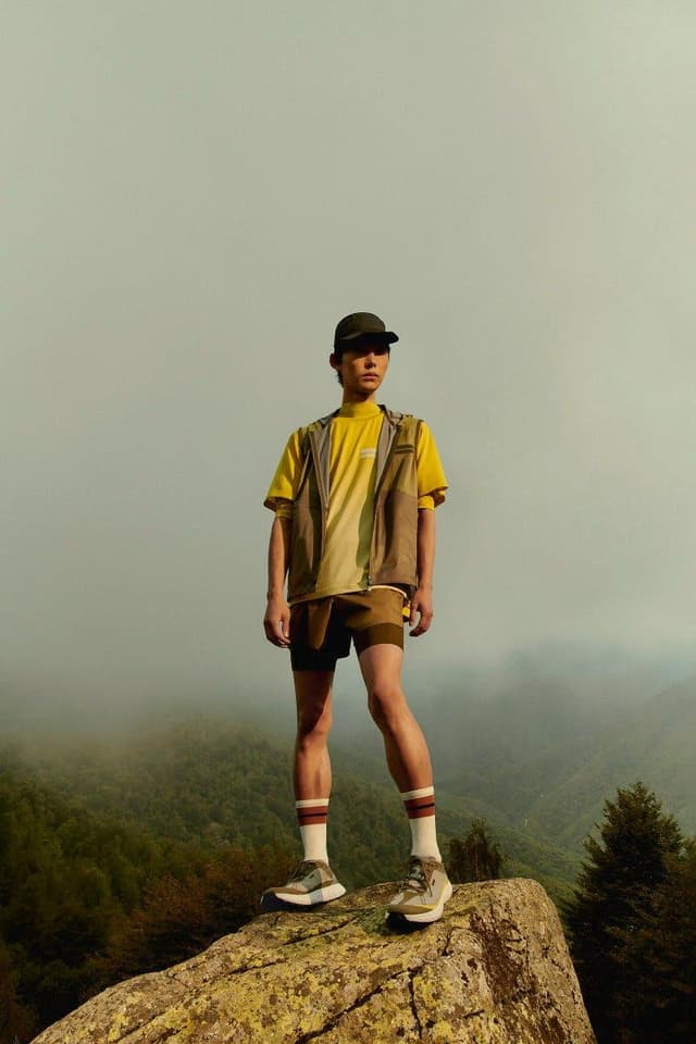 A young person in hiking attire stands on a rock overlooking a misty mountain range.