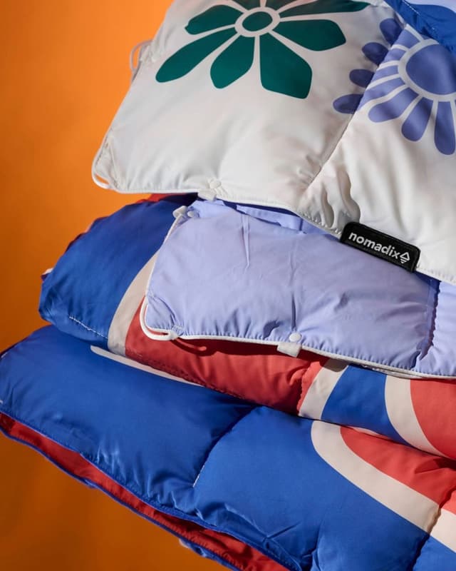 A stack of colorful quilted outdoor blankets, featuring floral and striped patterns, against an orange background.