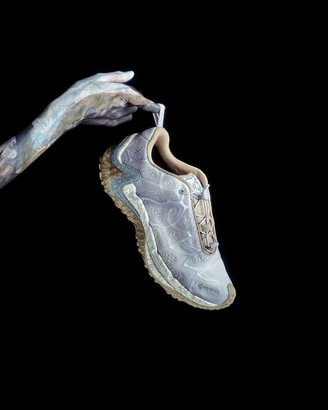 A hand painted white and brown holds a light grey and beige athletic shoe against a black background.