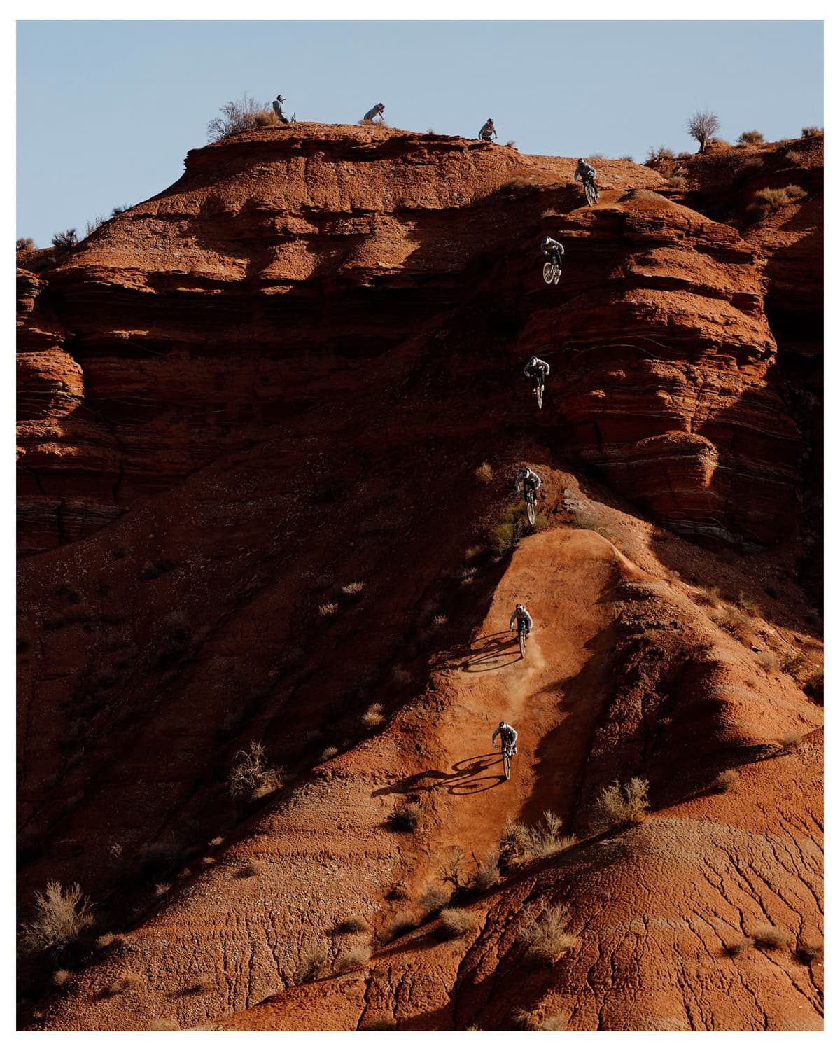 A sequence shot shows a mountain biker jumping and riding down a steep red rock desert mountain.