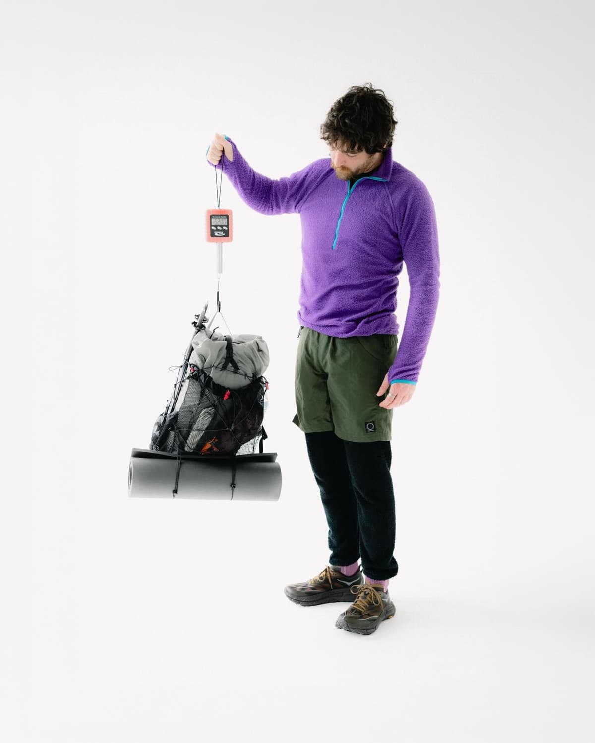 A man weighing a loaded backpack and sleeping pad with a digital scale.