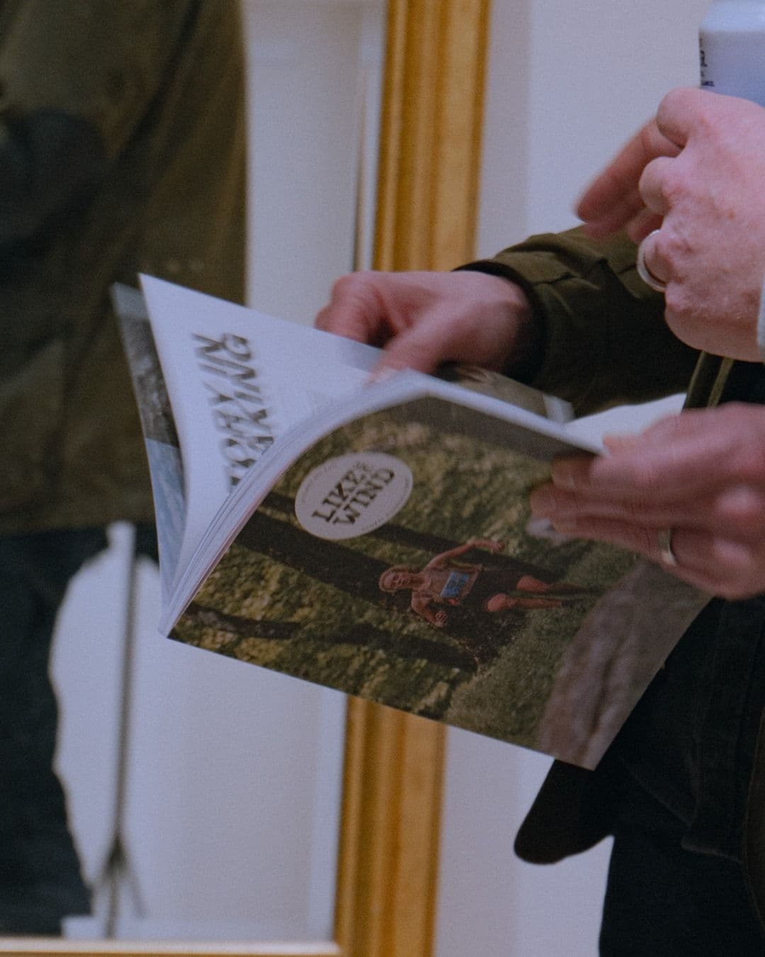 Hands hold and flip through a magazine titled "LIKE THE WIND" with a runner on its cover.