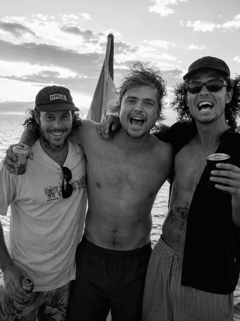 Black and white photo of three smiling men on a boat, two holding drinks.